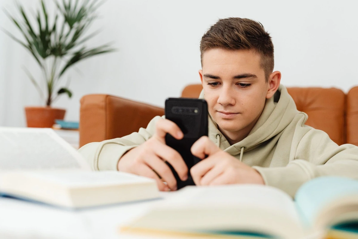 Joven consultando su teléfono móvil junto a unos libros.